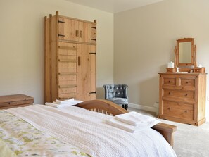 A bedroom with a bed, a wooden wardrobe, a dresser, and a chair.