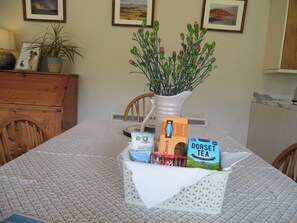 A dining table with a white tablecloth, a vase with green plants, and a basket containing food items.