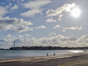 Une plage avec un phare en arrière-plan, un ciel dégagé et quelques personnes se promenant le long du rivage.