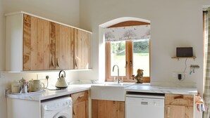 A compact kitchen with wooden cabinets, a washing machine, a dishwasher, and a window with a view of greenery.