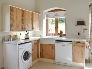 Cocina compacta con armarios de madera, lavadora, lavavajillas y ventana con vistas a zonas verdes.