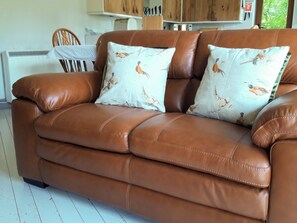 A brown leather sofa with two decorative pillows featuring bird patterns.
