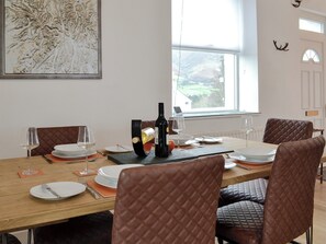 Comedor con una larga mesa dispuesta para cuatro, con sillas de cuero, platos blancos y copas de vino. Un cuadro adorna la pared, y una ventana ofrece vistas al exterior.
