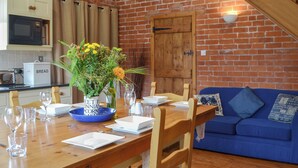 A dining area with a wooden table set for four, a blue sofa, and a brick wall. - 2 bedroom accommodation in Eardisland, near Leominster (Eardisland, near Leominster)