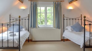 A room with two beds, a window with curtains, a radiator, and wooden beams on the ceiling. - 2 bedroom accommodation in Eardisland, near Leominster (Eardisland, near Leominster)