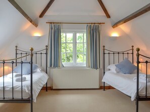 Une chambre avec deux lits, une fenêtre avec des rideaux, un radiateur et des poutres en bois au plafond.