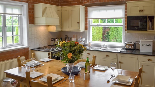 A kitchen with white cabinets, a dining table set for four, a window with a view of greenery, and a microwave above the counter. - 2 bedroom accommodation in Eardisland, near Leominster (Eardisland, near Leominster)