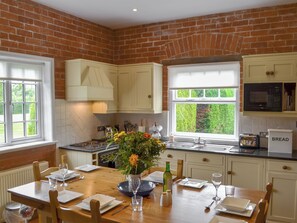 A kitchen with white cabinets, a dining table set for four, a window with a view of greenery, and a microwave above the counter.