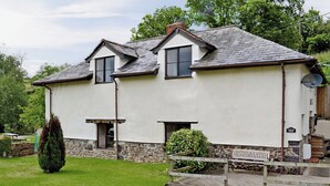 A two-story house with a stone foundation, a white exterior, and a grey roof.