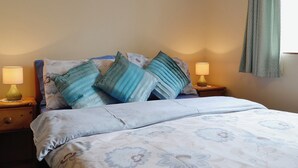 A neatly made bed with a floral-patterned bedspread, two bedside lamps, and a window with a green curtain.