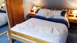 Ein ordentlich bezogenes Bett mit Handtüchern, einer Nachttischlampe und einem Nachttisch mit Büchern.