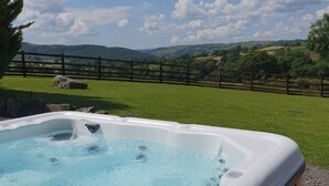 A hot tub in a grassy area with a wooden fence and hills in the background. - Y Dderwen at Brynglas Farm (Llanfair Caereinion)