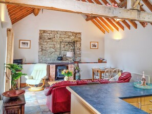 A cozy living room with a stone fireplace, a red sofa, a white armchair, and a dining area with a table and chairs. - Y Dderwen at Brynglas Farm (Llanfair Caereinion)