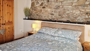 Un dormitorio con pared de piedra, armario de madera y colcha estampada.