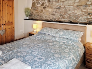 A bedroom with a stone wall, wooden wardrobe, and a floral bedspread.