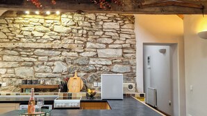 Una cocina con pared de piedra, vigas de madera, un reloj y una radio antigua.