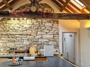 A kitchen with a stone wall, wooden beams, a clock, and a vintage radio.