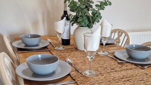A dining table set with bowls, wine glasses, and a bottle, surrounded by chairs and a plant. - Y Dderwen at Brynglas Farm (Llanfair Caereinion)