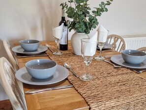 A dining table set with bowls, wine glasses, and a bottle, surrounded by chairs and a plant.