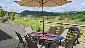 Un área de comedor al aire libre con una mesa preparada para seis personas, rodeada de sillas y cubierta por una sombrilla grande.
