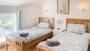 A double room with two wooden beds, a bedside table with a lamp, a mirror on the wall, and a window with curtains.