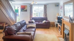 A living room with a staircase, two sofas, a fireplace, and a television.