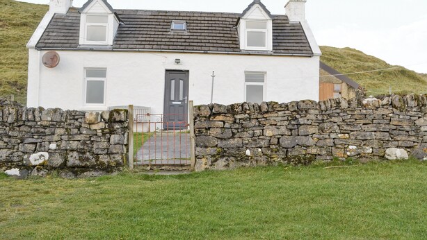 Une petite maison blanche avec un mur en pierre, une porte noire et une petite fenêtre.
