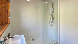 Une salle de bain moderne avec une douche à parois de verre, un lavabo blanc et une étagère en bois.