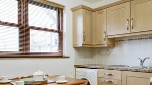 A compact kitchen with wooden cabinets, a washing machine, and a dining area with a table and chairs.