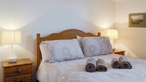 A neatly made bed with patterned bedding, two bedside lamps, a wooden nightstand with a drawer, and a framed picture on the wall.
