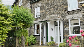 A stone building with a traditional design, featuring a green door, white windows, and a small porch with a lamp. - 3 bedroom accommodation in Windermere (Windermere)