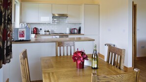 A modern kitchen with white cabinets, a wooden dining table, and a red flower vase. - 2 bedroom accommodation in Burgh le Marsh, near Skegness (Burgh le Marsh, near Skegness)