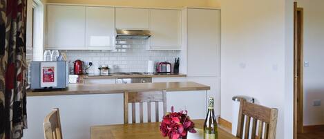 A modern kitchen with white cabinets, a wooden dining table, and a red flower vase.