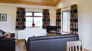 A living room with a sofa, a television, and a window with curtains. - 2 bedroom accommodation in Burgh le Marsh, near Skegness (Burgh le Marsh, near Skegness)