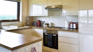 A modern kitchen with white cabinets, a stainless steel range hood, a built-in oven, and a window providing natural light. - 2 bedroom accommodation in Burgh le Marsh, near Skegness (Burgh le Marsh, near Skegness)