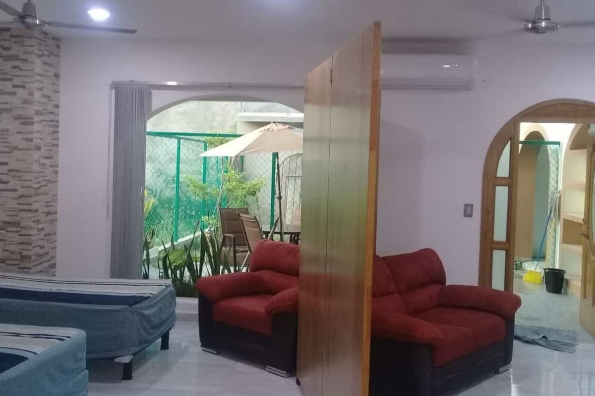 Ein modernes Wohnzimmer mit einem roten Sofa, einem blauen Sofa und einem Deckenventilator. Ein großes Fenster bietet Blick auf Grünflächen.
