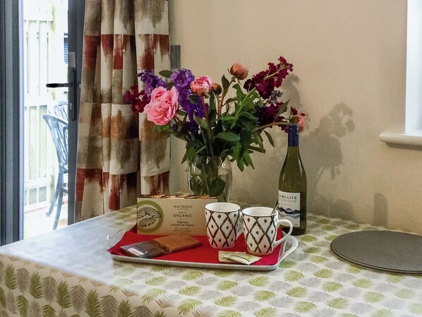 A table with a tray holding a bottle of wine, two cups, a box of Waitrose organic biscuits, and a vase with flowers.