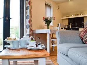 Un salon chaleureux avec un coin repas, un canapé, une table avec des aliments pour le petit-déjeuner, et une cuisine en arrière-plan.