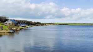 A lakeside view with a small dock, a building with a blue roof, and boats.