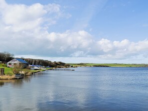Une vue sur un lac, avec un petit bâtiment en bois, des bateaux et une étendue d'eau calme.
