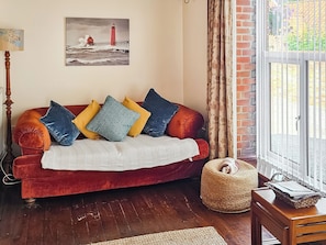 A cozy living room with a red sofa, a woven pouf, a wooden side table, and a painting of a lighthouse.