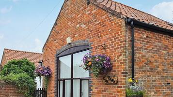 A brick building with a tiled roof, a large window, and flower baskets.