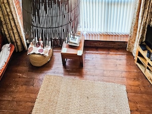 A cozy living room with a wooden floor, a woven rug, a small wooden table, and a television on a wooden stand.