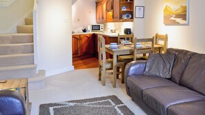 A cozy living room with a brown leather sofa, a wooden dining table with chairs, and a kitchen area with wooden cabinets and a microwave. - 1 bedroom accommodation in Windermere (Windermere)