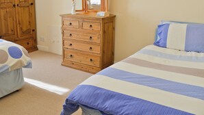 A bedroom with a wooden dresser, a bed with striped bedding, and a painting on the wall. - 1 bedroom accommodation in Windermere (Windermere)