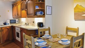 A kitchen with wooden cabinets, a microwave, a stove, and a dining table set for four with blue and white plates and bowls. - 1 bedroom accommodation in Windermere (Windermere)