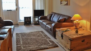 A living room with a leather sofa, a wooden chest, a lamp, and a television. - 1 bedroom accommodation in Windermere (Windermere)