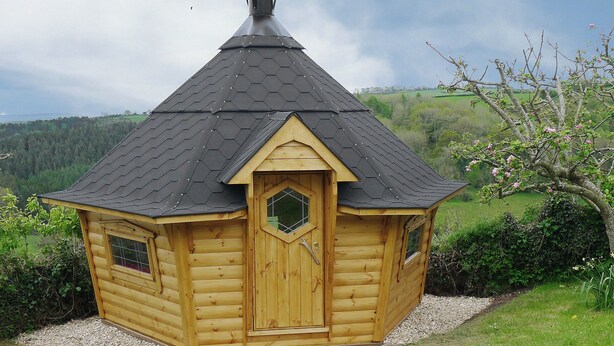 Eine Holzhütte mit einem kegelförmigen Dach, einer mittleren Tür und zwei Fenstern an der Seite.