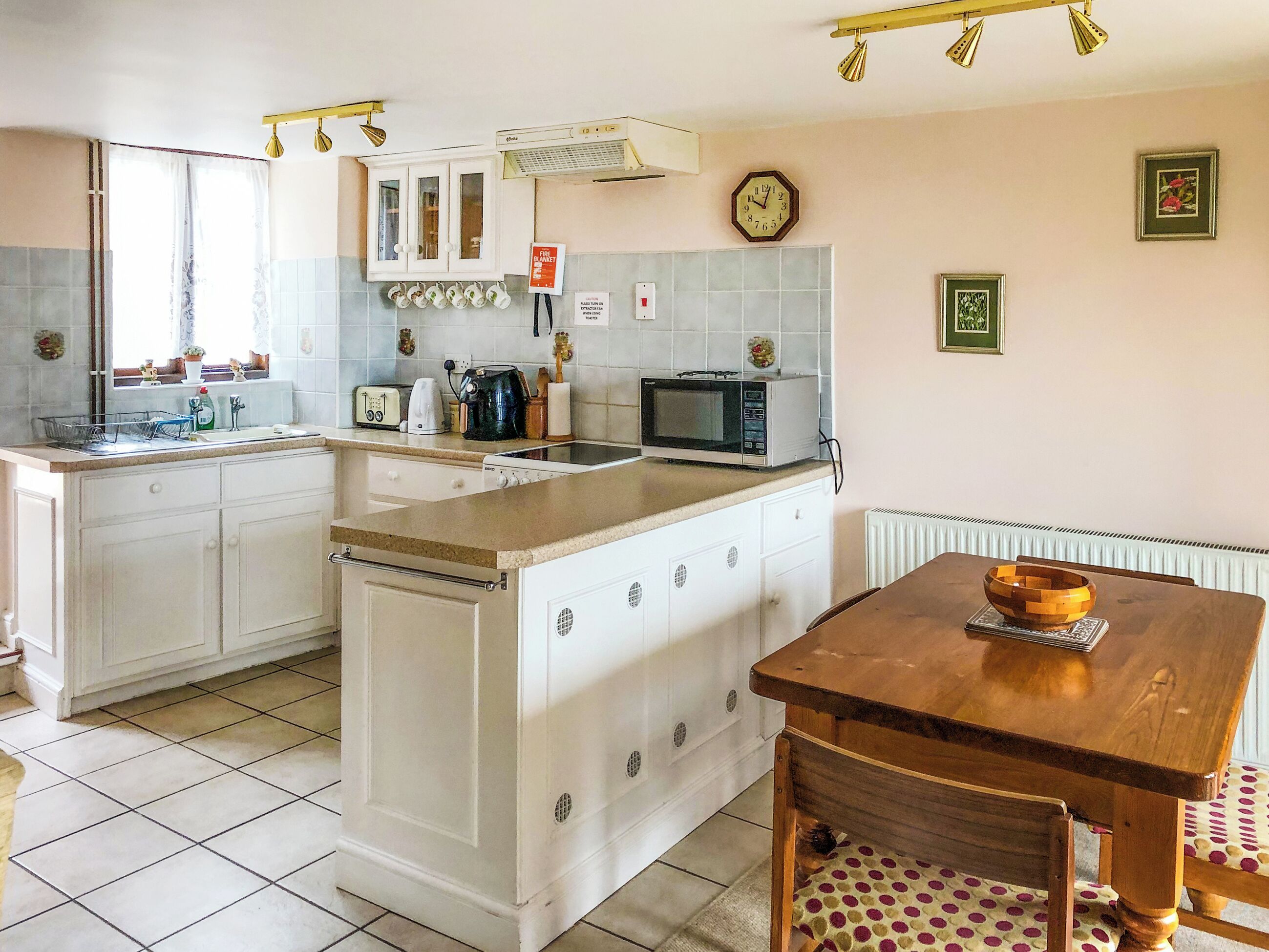 Een keuken met witte kasten, een houten eettafel en een betegelde vloer.