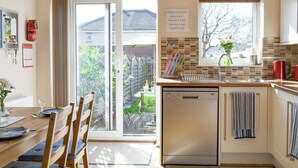 A modern kitchen with a dishwasher, a dining area with a table and chairs, and a view of the backyard through a sliding door. - 2 bedroom accommodation in Scarborough (Scarborough)